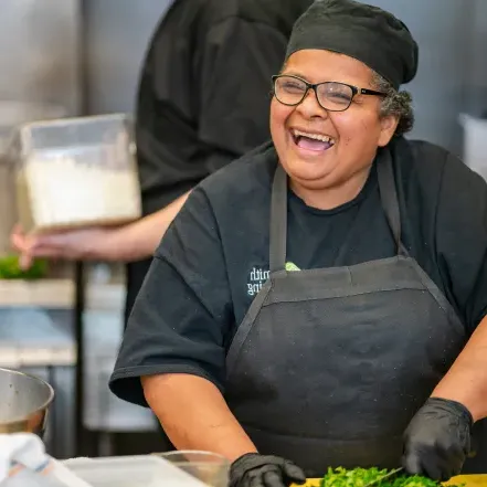 Maria Aguilar smilies while chopping vegetables in the Chase-Duckett kitchen